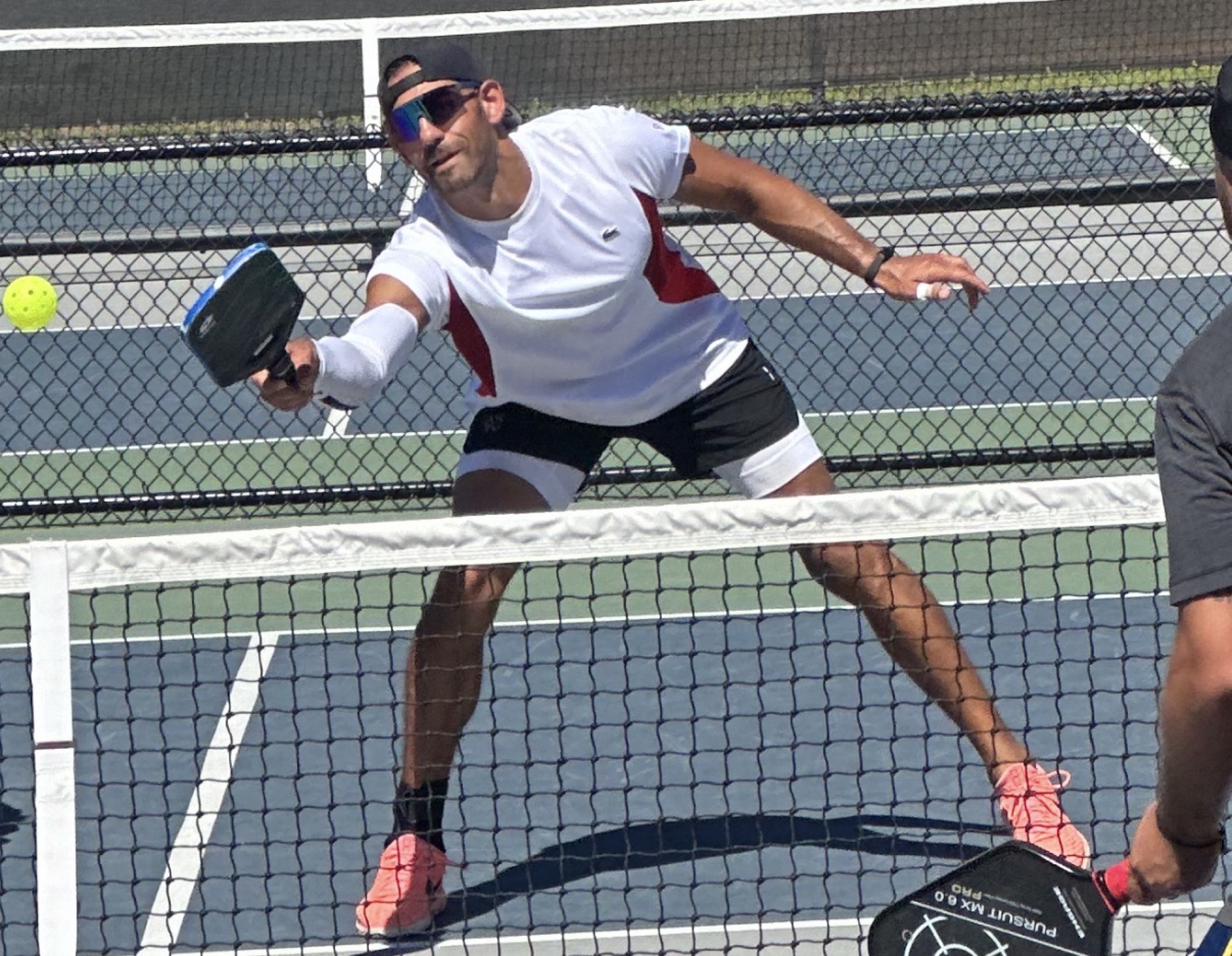 MO reaching for a volley at the net on an outdoor pickleball court